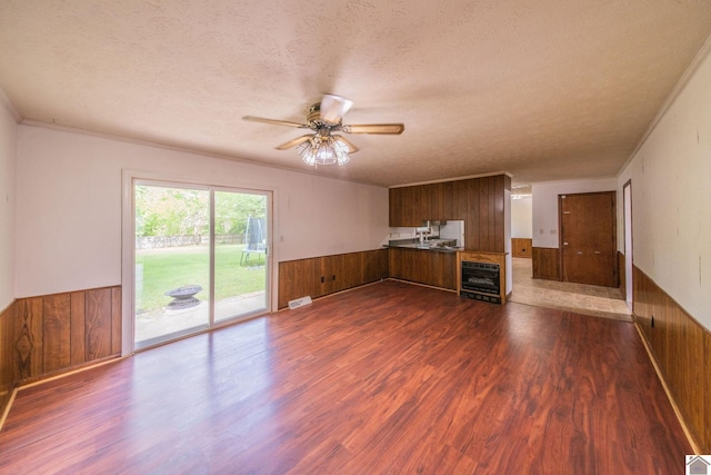 unfurnished living room featuring wood walls, a textured ceiling, dark wood-type flooring, and wainscoting