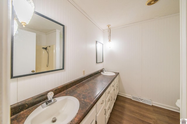 full bath featuring a sink, double vanity, visible vents, baseboards, and wood finished floors