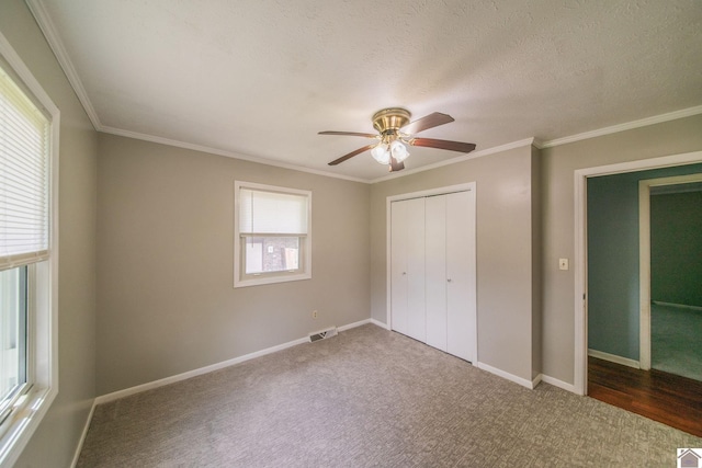 unfurnished bedroom with a closet, ornamental molding, carpet flooring, baseboards, and visible vents