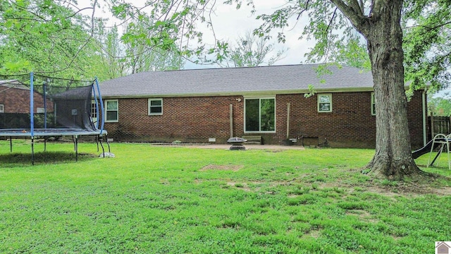 back of property featuring a lawn, a patio area, brick siding, and a trampoline