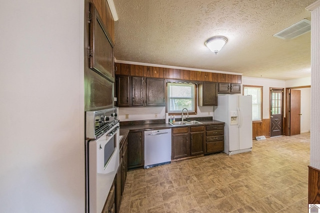 kitchen featuring white appliances, dark countertops, a sink, visible vents, and a textured ceiling