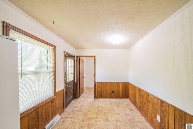 empty room featuring wooden walls, a wainscoted wall, visible vents, and a textured ceiling