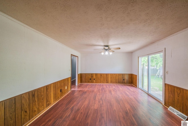 empty room with wooden walls, crown molding, wainscoting, and wood finished floors