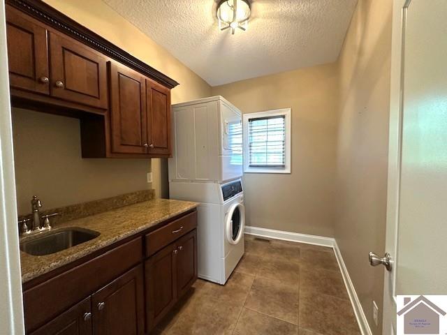 57 Rippling Creek Dr, Murray, KY 42071 - clothes washing area featuring a textured ceiling, a sink, baseboards, stacked washing maching and dryer, and cabinet space