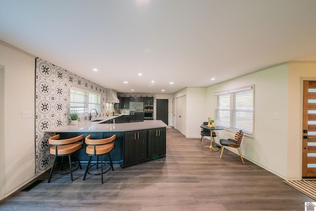 kitchen featuring recessed lighting, stainless steel fridge, a sink, a peninsula, and premium range hood