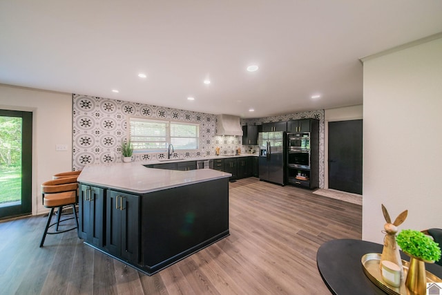 kitchen with a sink, stainless steel refrigerator with ice dispenser, light wood-style flooring, a peninsula, and plenty of natural light