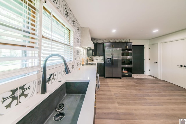 kitchen featuring light wood-style floors, appliances with stainless steel finishes, light countertops, dark cabinetry, and a sink