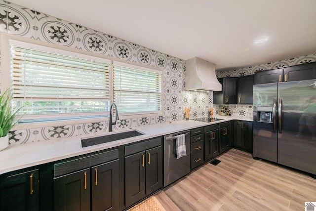 kitchen featuring light wood-style flooring, appliances with stainless steel finishes, light countertops, a sink, and premium range hood