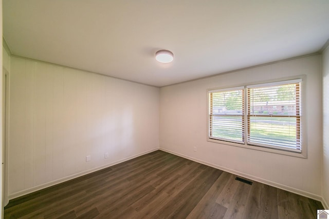 empty room featuring dark wood-type flooring, visible vents, and baseboards