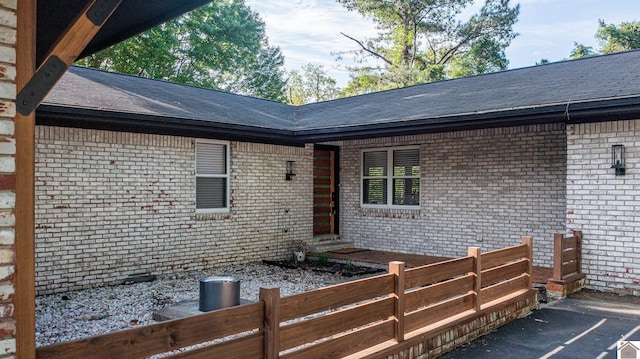 exterior space with brick siding, fence, and a shingled roof
