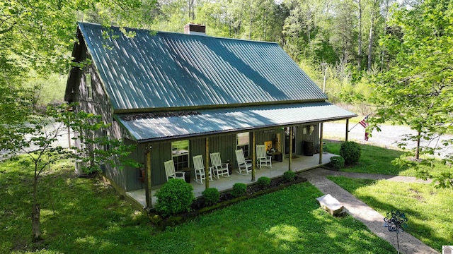 back of house featuring board and batten siding, a chimney, a patio area, metal roof, and a lawn