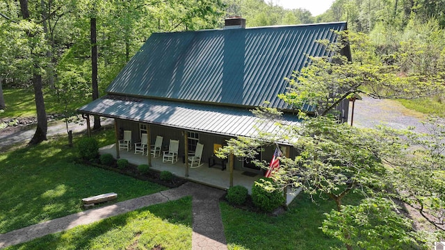 view of front of property featuring a wooded view, a patio, a chimney, metal roof, and a front yard