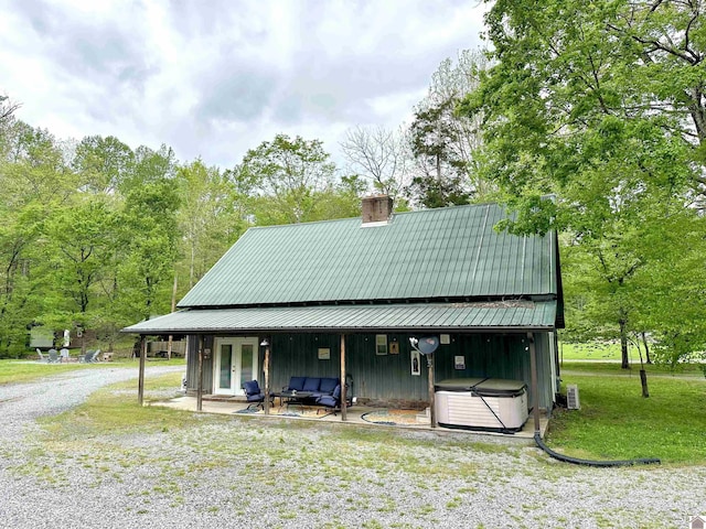 rear view of house featuring a patio area, a hot tub, board and batten siding, a chimney, and french doors