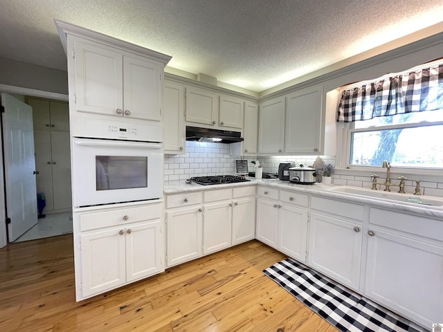 11189 E State Route 94, Murray, KY 42071 - kitchen with white oven, under cabinet range hood, black gas stovetop, a sink, and a textured ceiling