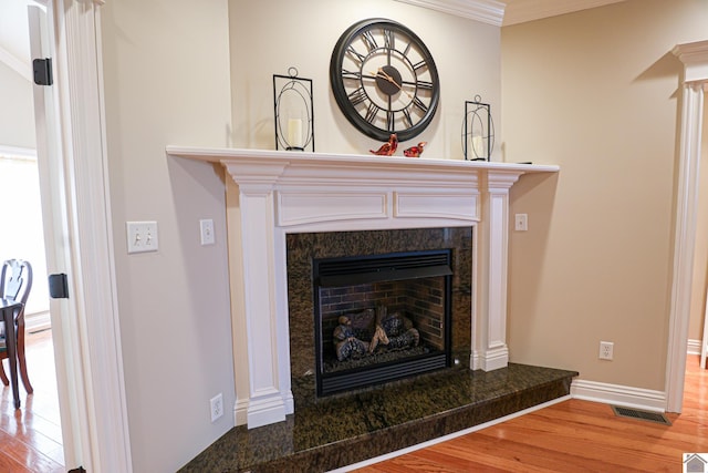 room details with crown molding, visible vents, a high end fireplace, baseboards, and wood finished floors