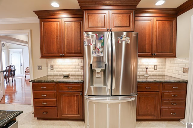 kitchen with dark stone counters, light tile patterned floors, stainless steel fridge with ice dispenser, brown cabinetry, and backsplash