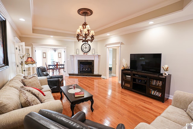 living room featuring crown molding, light wood-style flooring, a chandelier, a tray ceiling, and recessed lighting