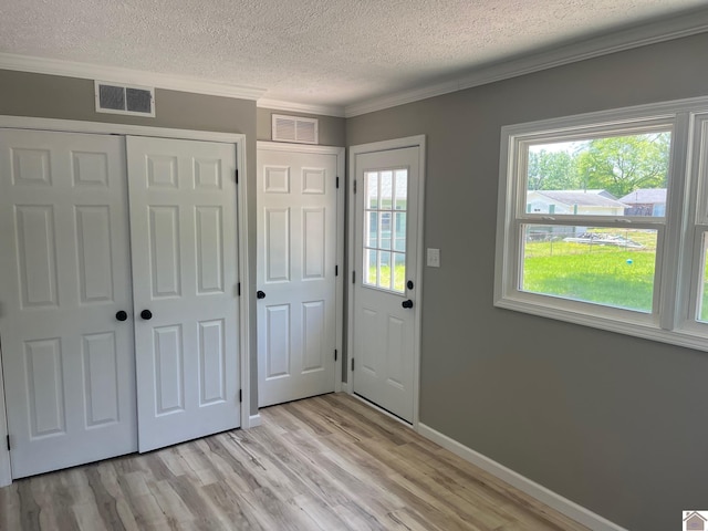 foyer with visible vents, light wood-style flooring, a textured ceiling, and crown molding