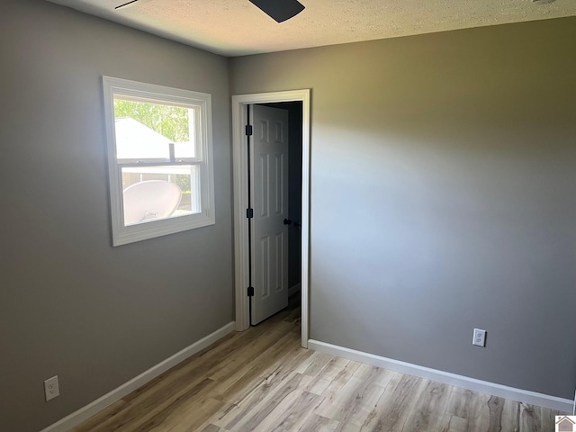 unfurnished room featuring baseboards, a ceiling fan, a textured ceiling, and light wood-style flooring