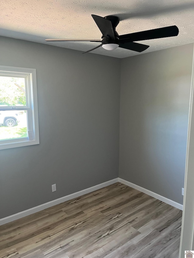 spare room featuring a textured ceiling, wood finished floors, ceiling fan, and baseboards