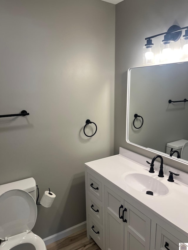 half bath featuring wood finished floors, vanity, toilet, and baseboards