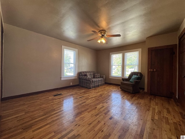 living area with baseboards, visible vents, wood finished floors, and ceiling fan