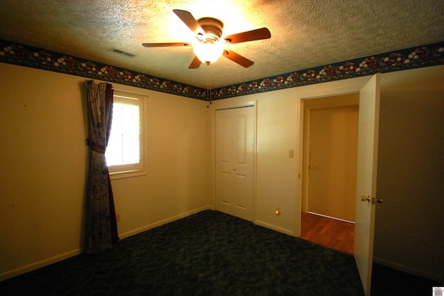 carpeted empty room featuring a textured ceiling, ceiling fan, and visible vents