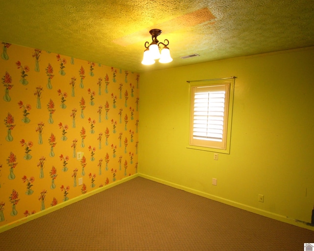 carpeted spare room with a textured ceiling, an inviting chandelier, and visible vents