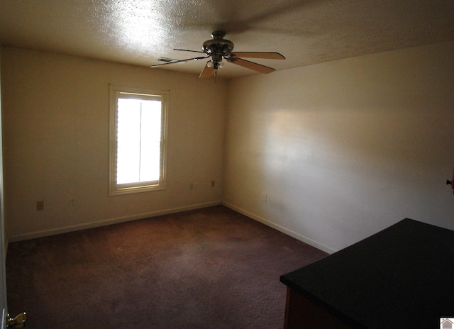 unfurnished room with dark carpet, a ceiling fan, baseboards, and a textured ceiling