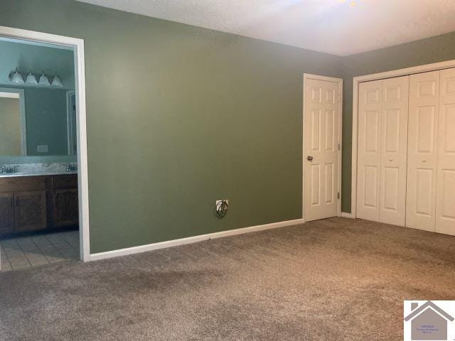 unfurnished bedroom featuring carpet flooring, a closet, ensuite bath, baseboards, and a sink