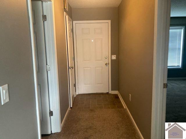 hall featuring dark colored carpet and baseboards