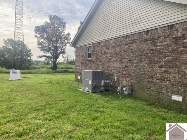 view of side of property featuring central AC unit, brick siding, and a yard