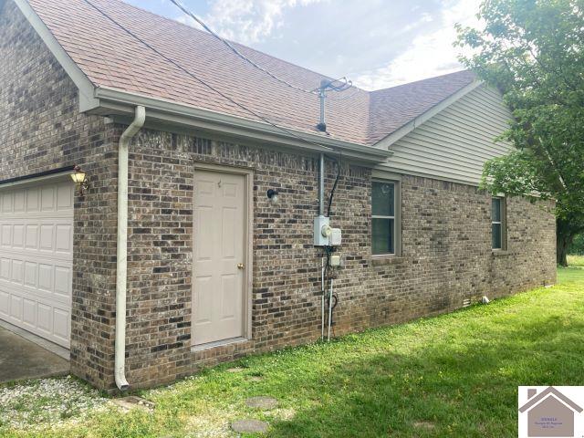 view of side of home with brick siding, a garage, roof with shingles, and a yard