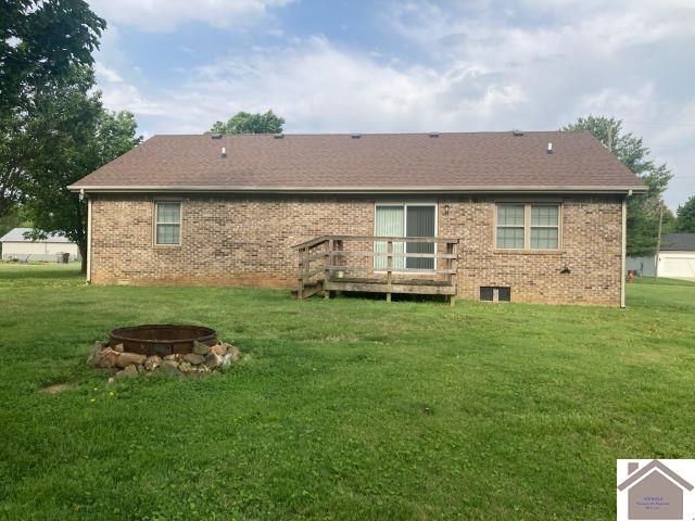 rear view of house with a fire pit, brick siding, and a lawn