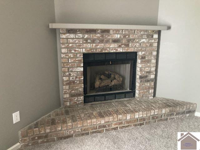 detailed view of a brick fireplace, carpet floors, and baseboards