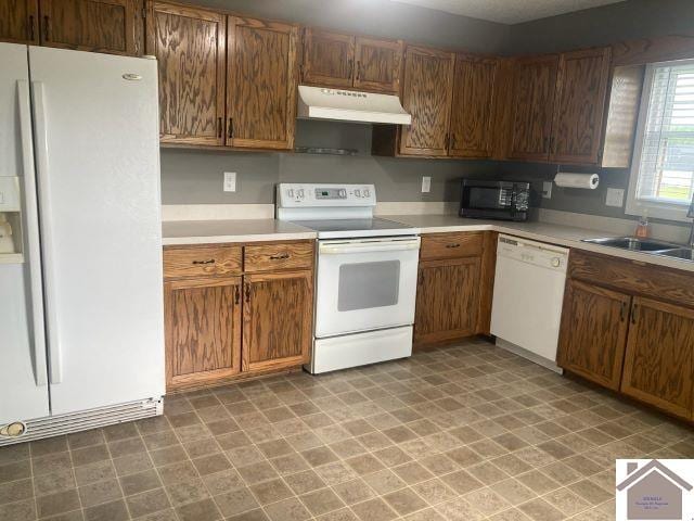 kitchen with white appliances, under cabinet range hood, a sink, light countertops, and light floors