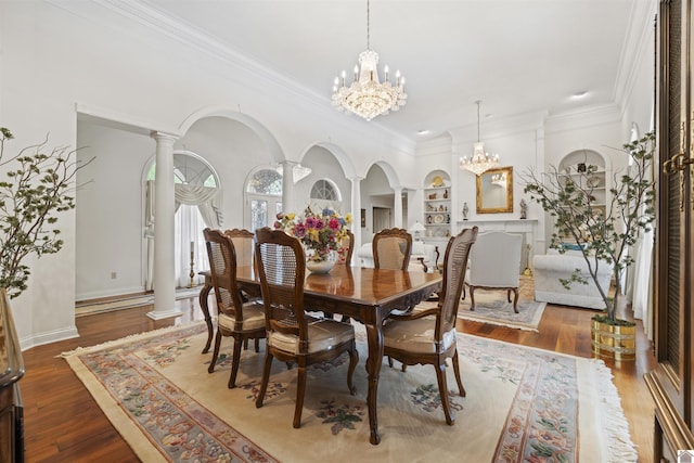 dining room featuring arched walkways, a chandelier, built in features, decorative columns, and ornamental molding