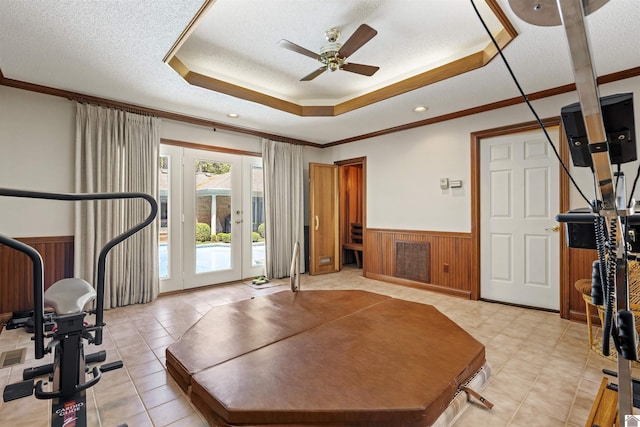 workout room featuring a ceiling fan, a textured ceiling, crown molding, a wainscoted wall, and a raised ceiling