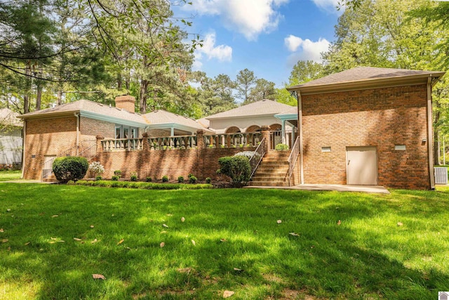rear view of house featuring a lawn, a deck, stairway, and brick siding