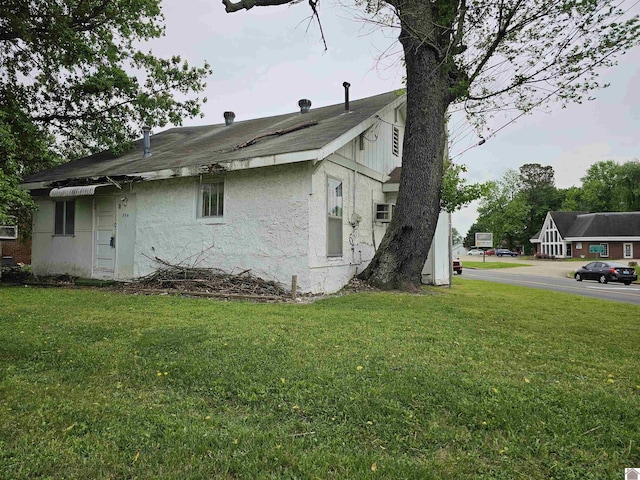 view of home's exterior with a lawn, a shingled roof, and stucco siding
