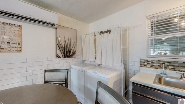 clothes washing area featuring a wall unit AC, laundry area, tile walls, washing machine and dryer, and a sink