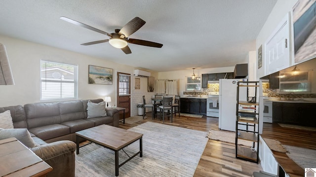 living area featuring a ceiling fan, light wood finished floors, a textured ceiling, and a wall mounted AC