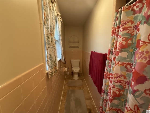 full bathroom with wainscoting, tile patterned floors, toilet, and tile walls