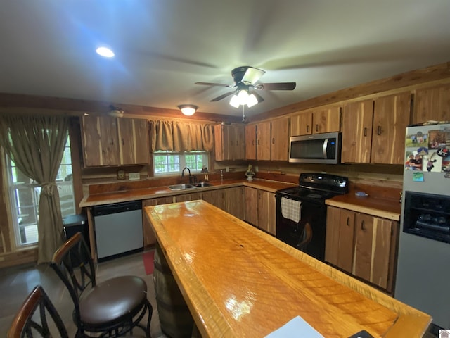 kitchen with ceiling fan, brown cabinets, a sink, wood counters, and stainless steel appliances