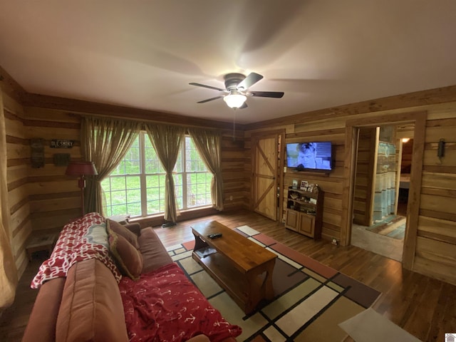 living area featuring a ceiling fan, wood walls, and wood finished floors