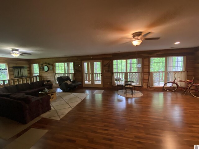 living area with plenty of natural light, a ceiling fan, wood finished floors, and wood walls