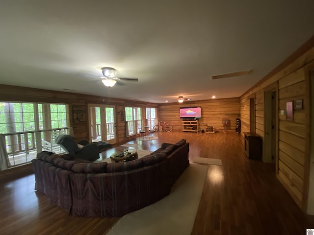 living room with ceiling fan, wood finished floors, and wooden walls