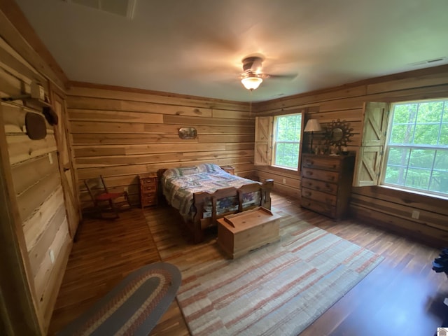 bedroom featuring wooden walls, a ceiling fan, visible vents, and wood finished floors