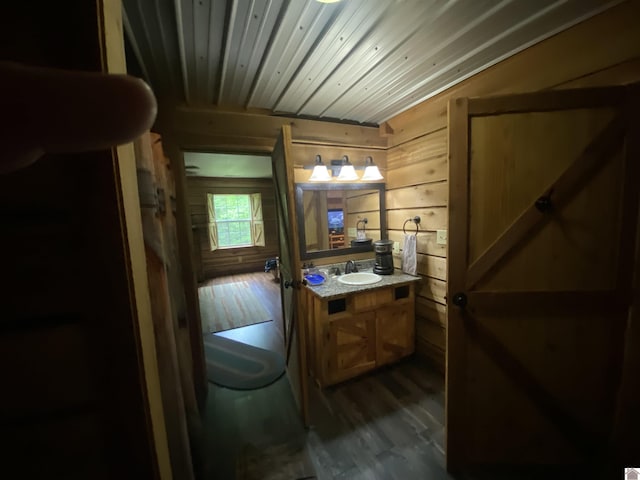 half bathroom with wood walls, wood finished floors, wooden ceiling, vanity, and toilet