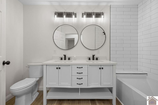 bathroom featuring double vanity, a sink, wood finished floors, and toilet